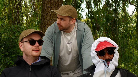 Drei junge Männer tragen extragroße Dad Hats von BigBrains. Zwei tragen die grüne Cap, einer die rote Cap. Im Hintergrund sind Bäume, Sträucher und Natur zu sehen.