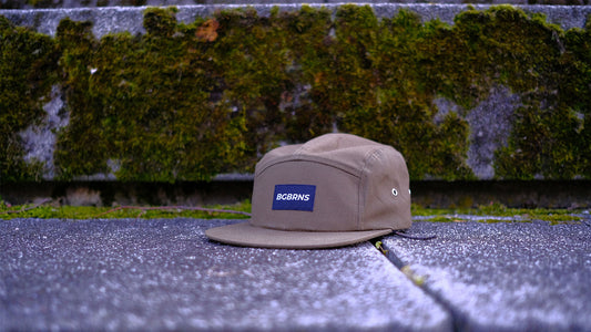Die extragroße Fivepanel Cap von BigBrains liegt auf einer Steinplatte. Im Hintergrund ist grünes Gewächs.