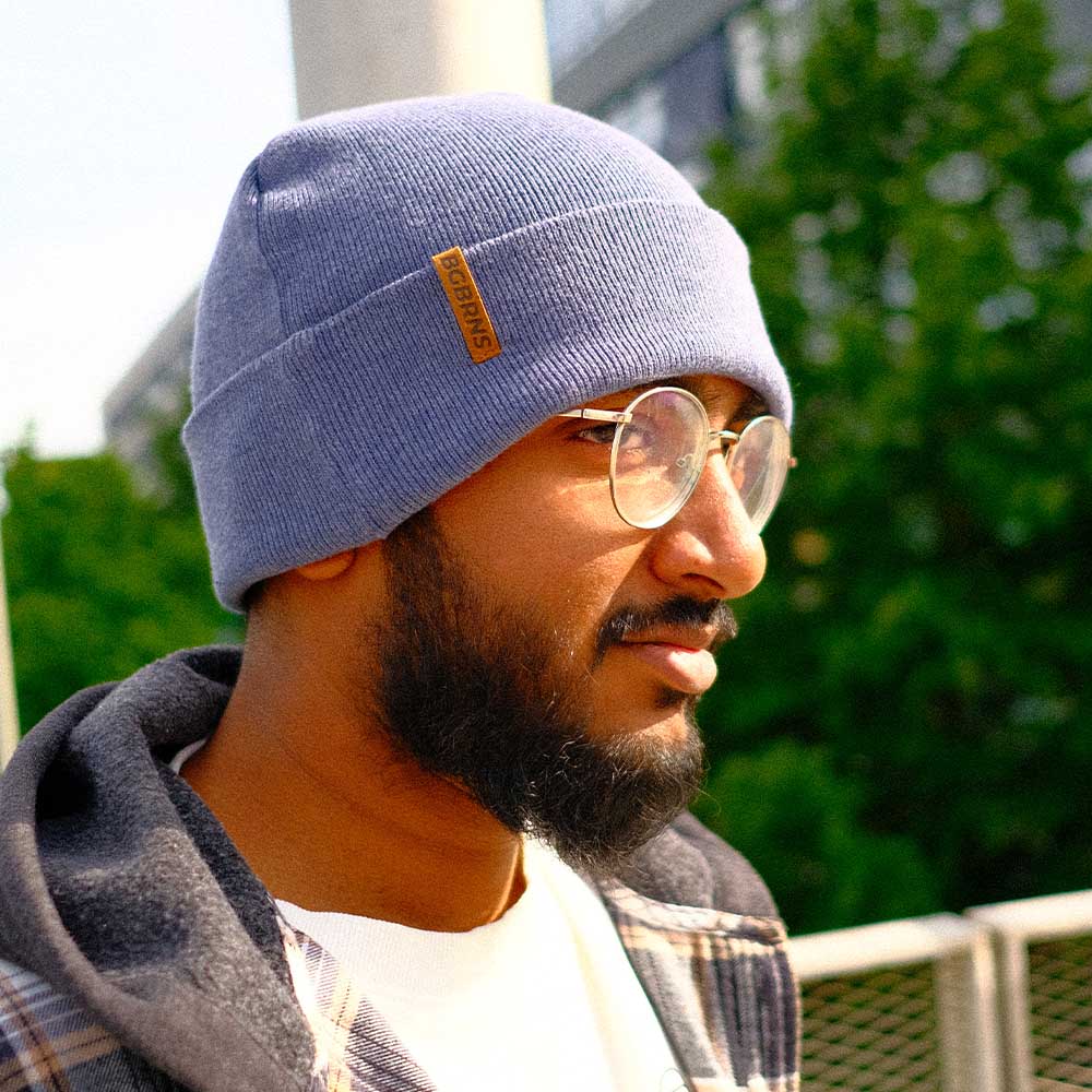Junger Mann trägt die extragroße oversize BigBrains Co. Snowy Blue Beanie Mütze. Er steht in Grünen und schaut rechts an der Kamera vorbei.