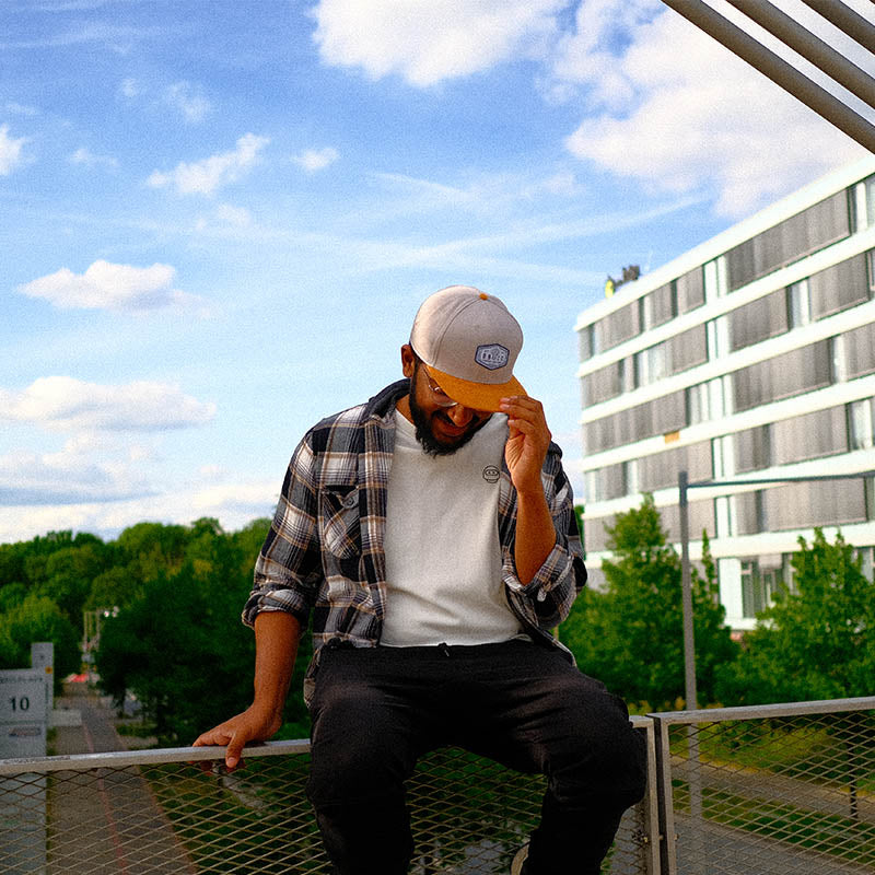 Ein Mann sitzt auf einem Geländer einer Brücke. Er trägt die extragroße oversize Snapback Cap von BigBrains Co.