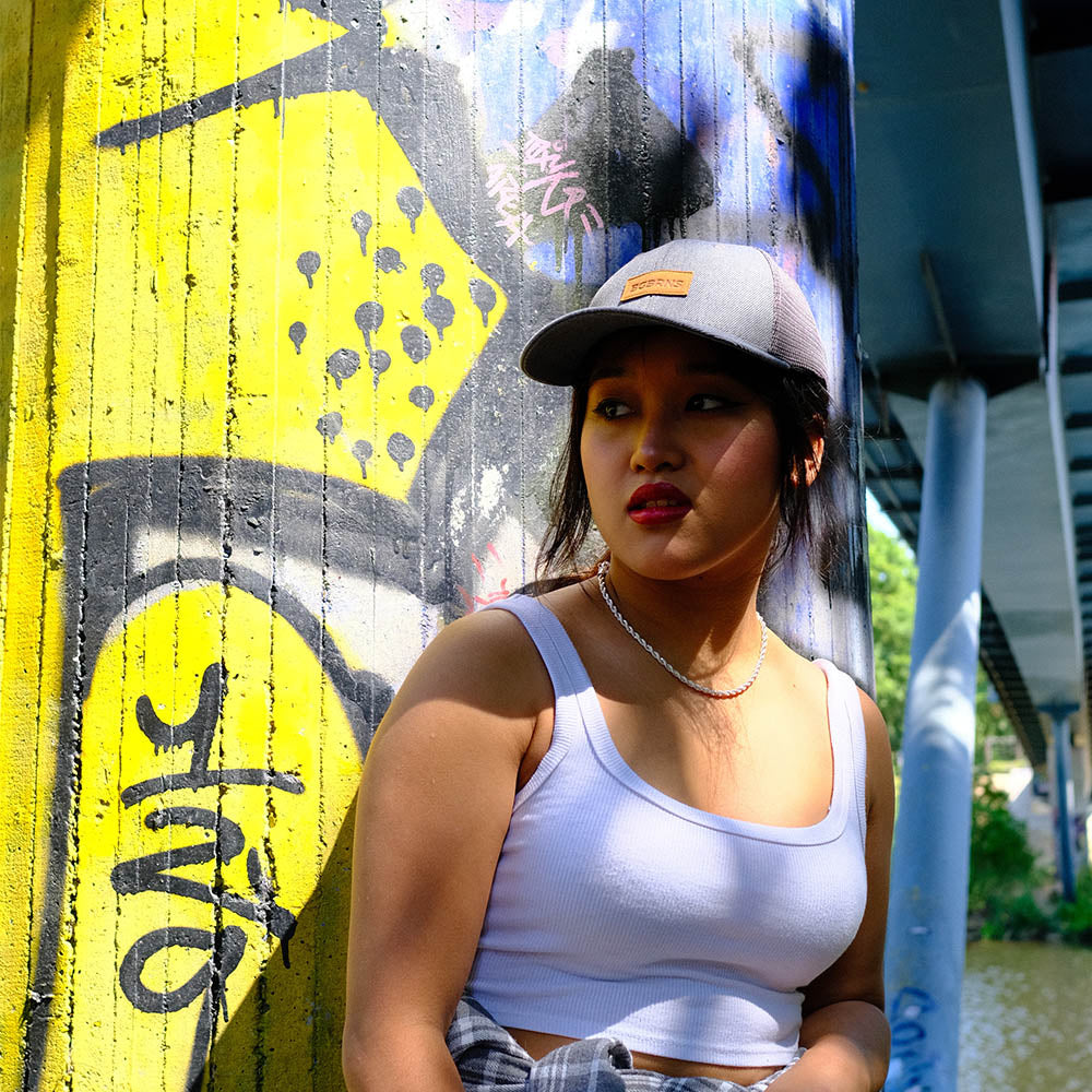 Portrait einer jungen Frau. Sie schaut links an der Kamera vorbei. Sie trägt ein weißes Top und eine XXL Trucker Cap von BigBrains auf ihrem Kopf.