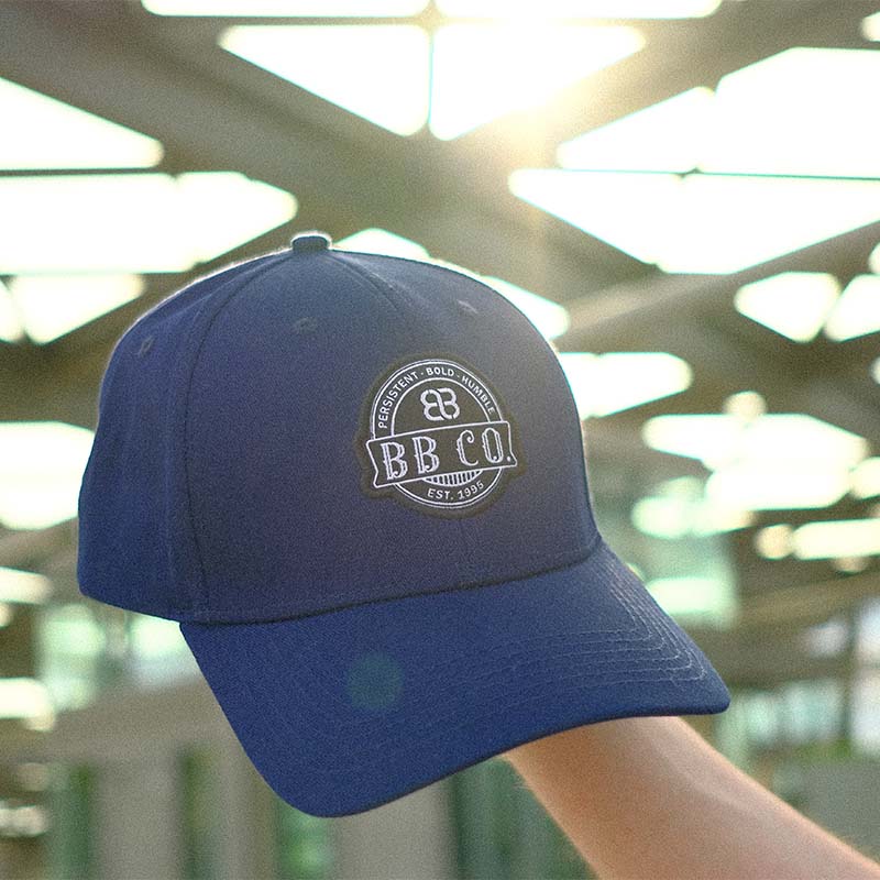 Die extragroße blaue Basecap von BigBrains Co. wird in der Hand in die Sonne gehalten.