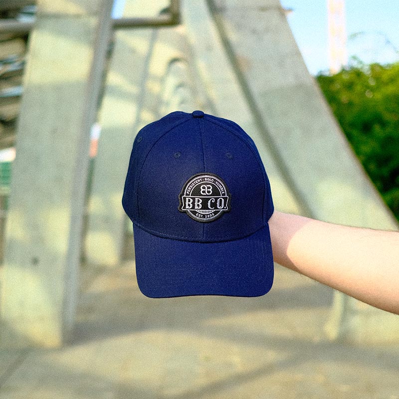Übergroße Baseball Cap von BigBrains Co. wird in der Nahaufnahme in das Kamerabild gehalten.