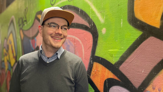 Portrait von Niklas Hermsdorf mit grauer BigBrains Co. XXL Snapback Cappie vor einer Grafitti Wand.