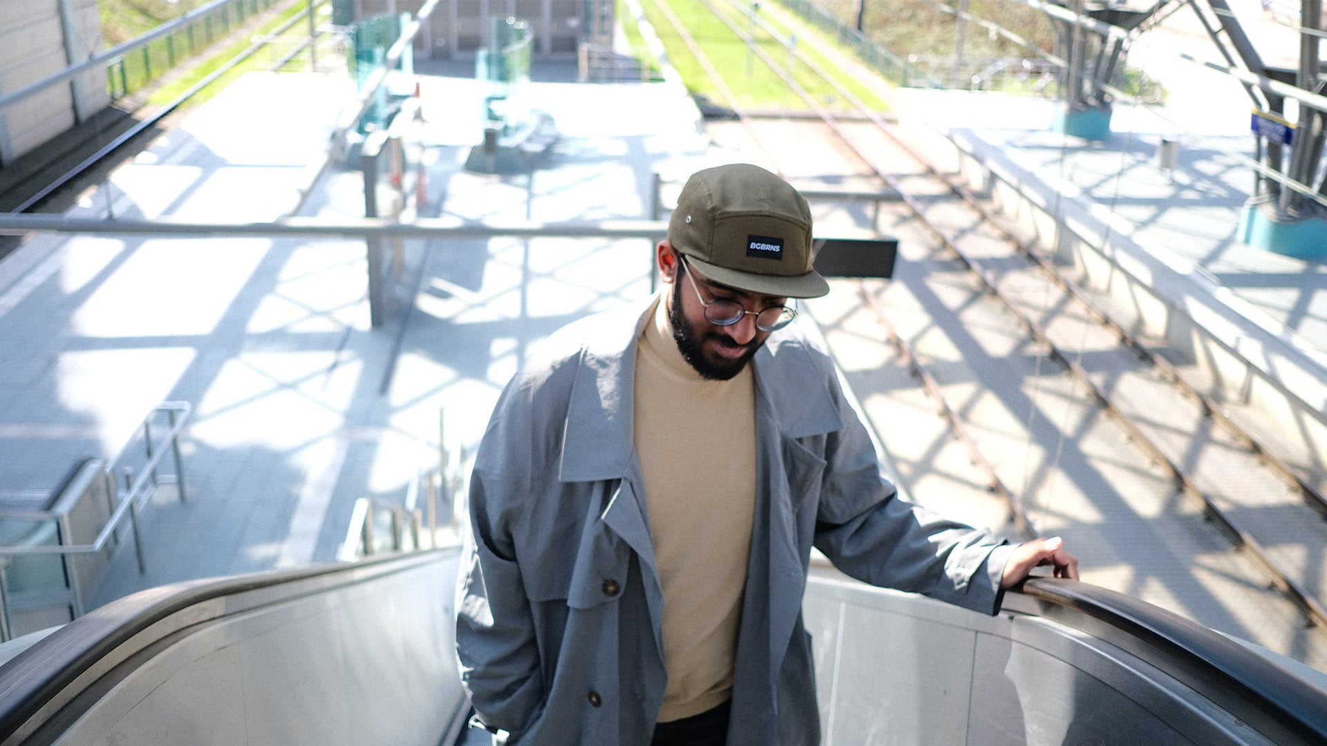 Ein junger Mann geht eine Rolltreppe hinauf. Er trägt die dunkelgrüne Fivepanel Cap für große Köpfe von BigBrains Co.