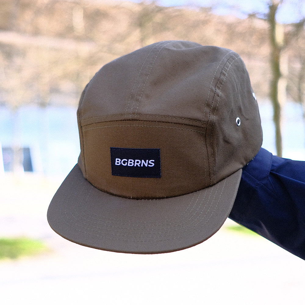 Die XL Fivepanel Cap von BigBrains wird von einer Person in die Luft gehalten. Die Cap hat Metallösen an der Seite.