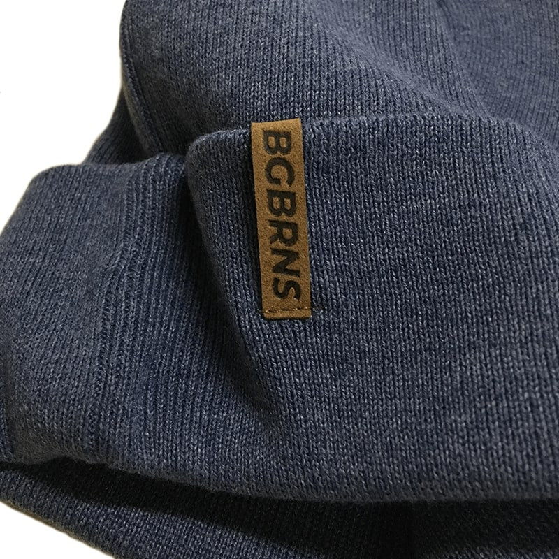Nahaufnahme des BigBrains Co. Logos "BGBRNS"-Aufnäher auf der extragroßen blaugrauen Beanie Mütze.